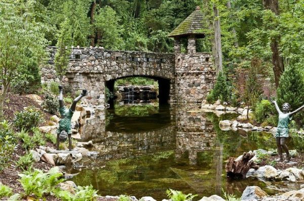 Large Reflecting Pond with Stone Bridge (Long Island/NY): The stone bridge with turret creates a stunning pond reflection in its crystal clear water. The water stays this way because we used a natural ecosystem to keep it clean. There is a large bog filter at the waterfall on one end, with a 3,000 gallon pondless reservoir with two 20,000 GPH pumps feeding the waterfall.
