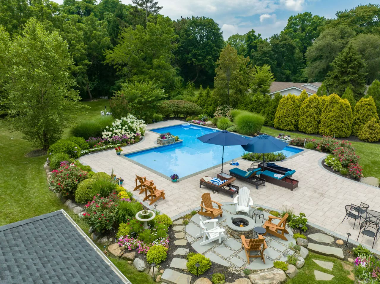Aerial view of a rectangular pool with paver patio, fire pit circle and lush planting beds