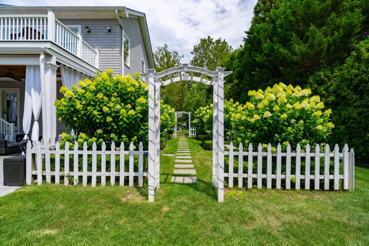 White arbor and picket fence opening onto a stepping-stone walk lined with hydrangeas