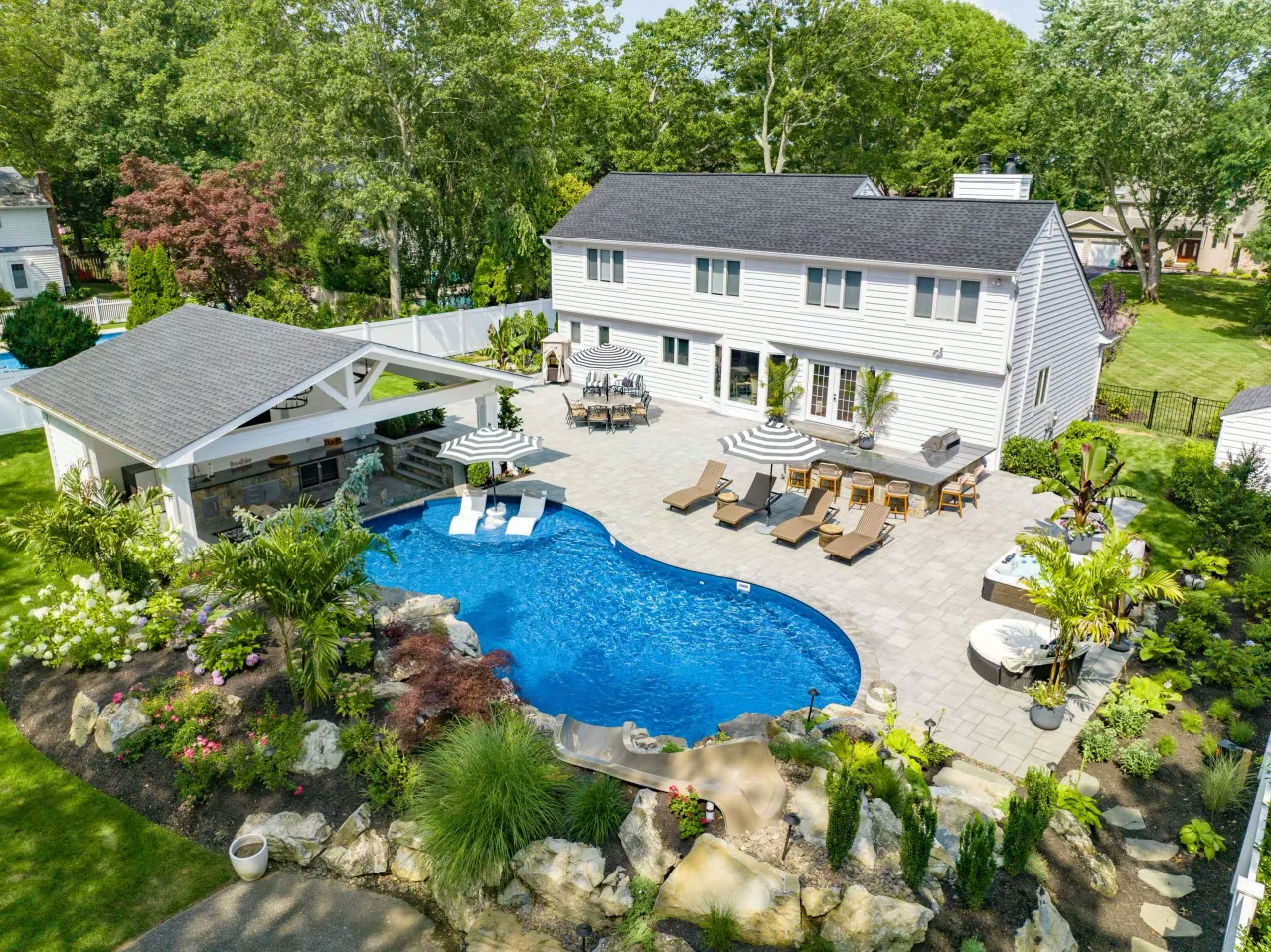 Aerial view of a complete backyard with freeform pool, slide, waterfalls, outdoor kitchen and pavilion