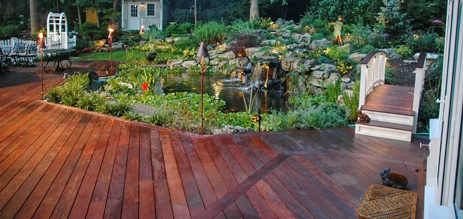 Hardwood deck bordering a pond with waterfall, lighting and garden bridge