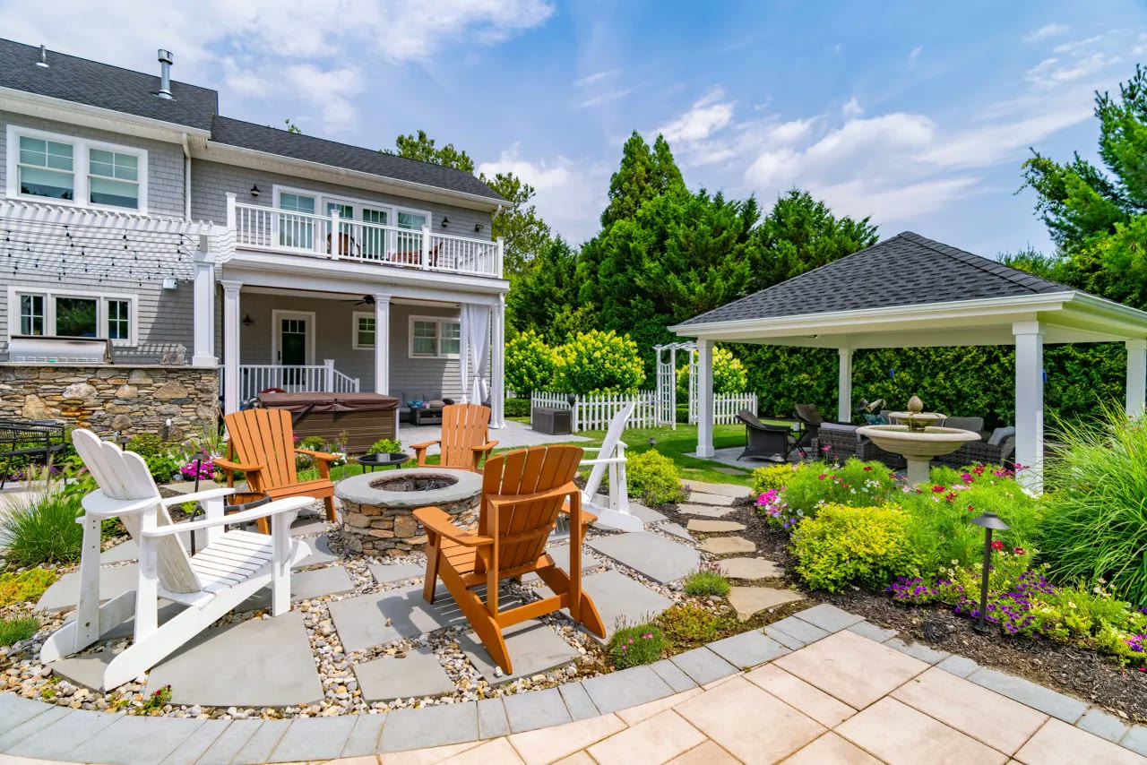 Stone fire pit and Adirondack chairs on a flagstone terrace beside a pavilion and hot tub