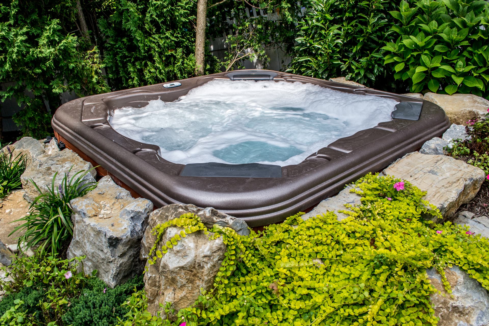 Hot tub running with jets surrounded by boulders and lush planting