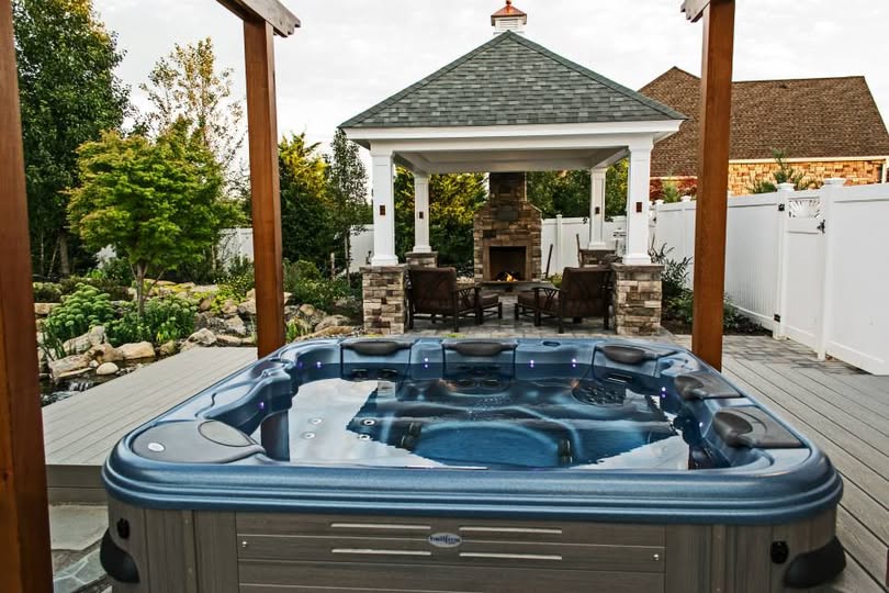 Hot tub on a wood deck beside a covered gazebo with stone fireplace