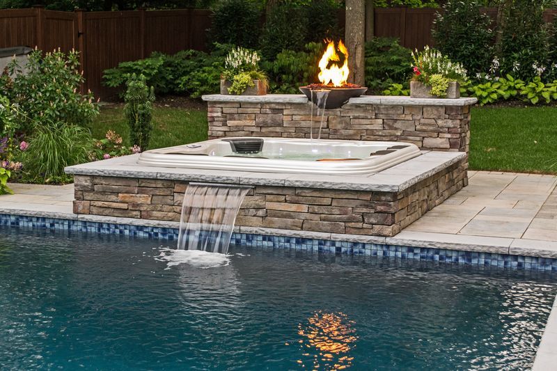 Spa with stone waterfall spilling into a pool beneath a lit fire bowl