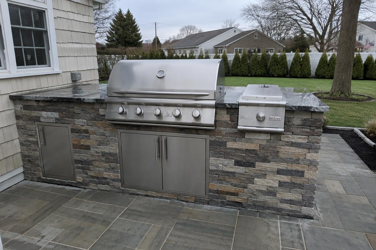 Built-in stainless grill and side burner in a stone outdoor kitchen