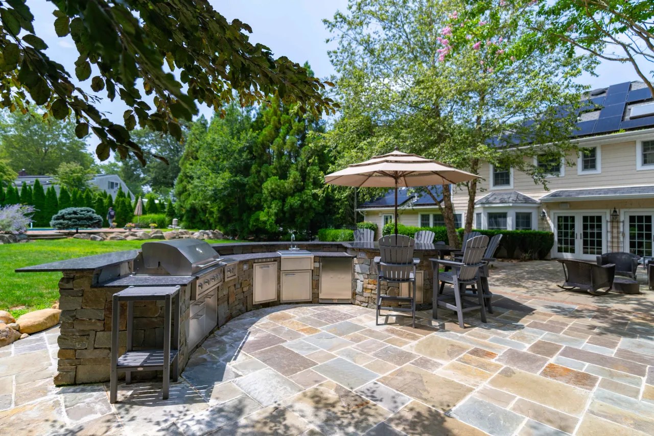 Stone outdoor kitchen with stainless built-in grill, sink and curved granite bar counter