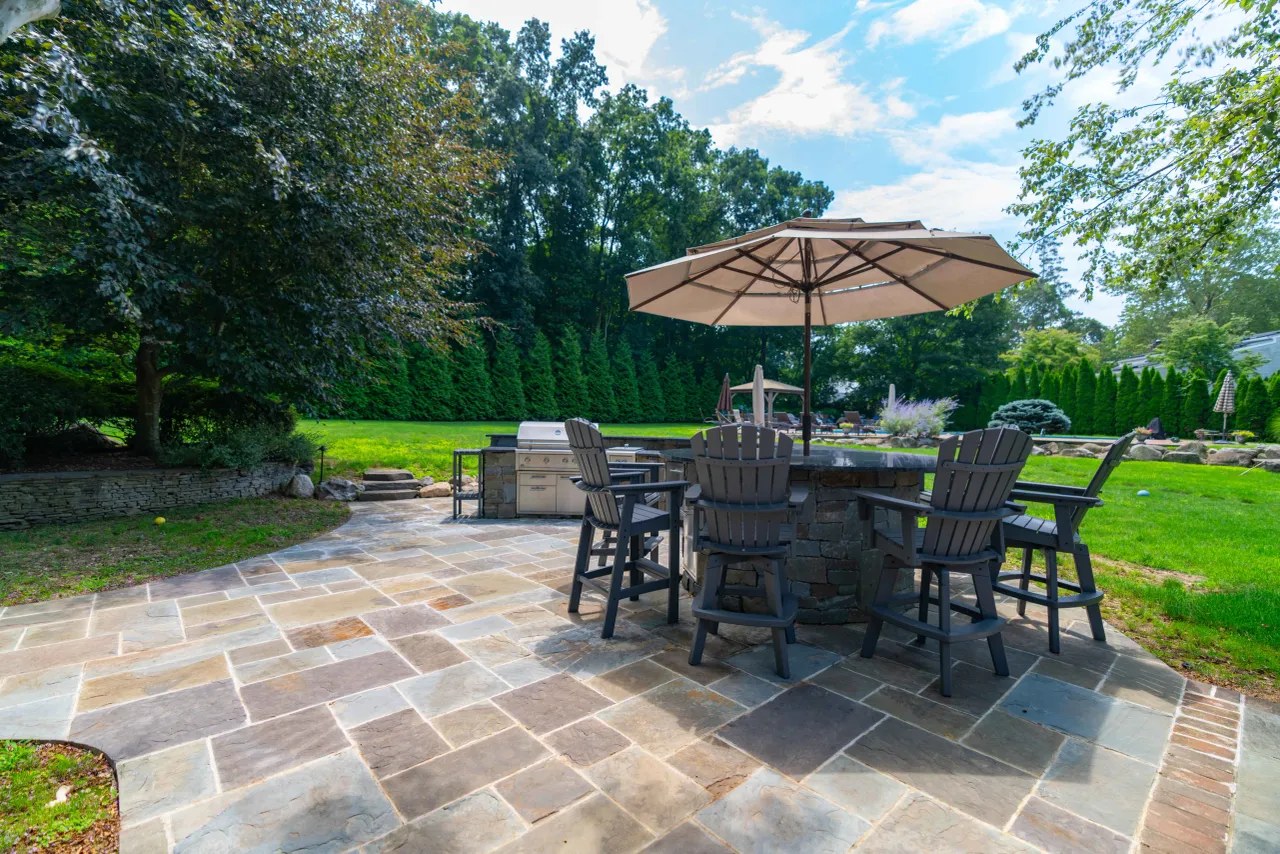 Curved stone outdoor bar with granite top, umbrella and bar seating beside the pool