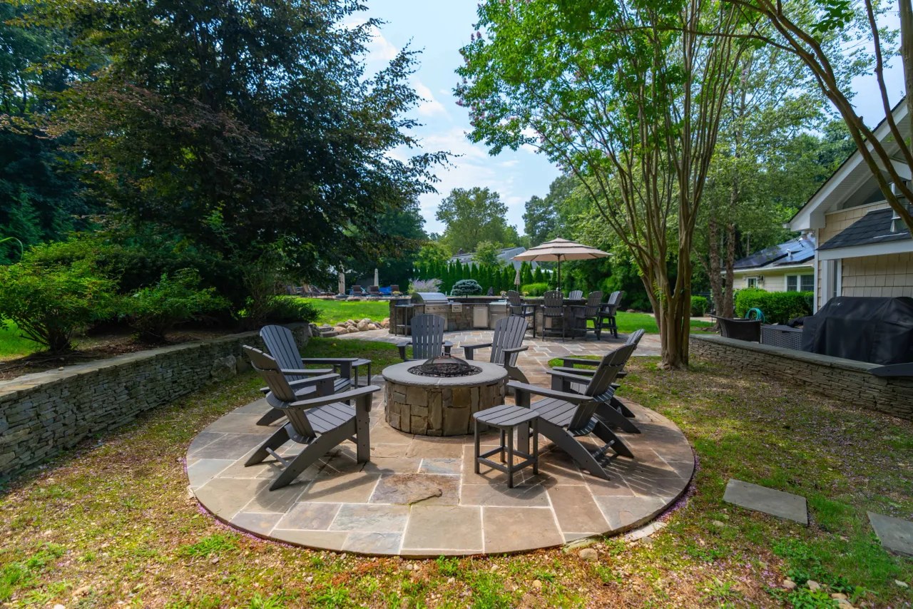 Stone fire pit circle with Adirondack chairs and seat walls, outdoor kitchen beyond