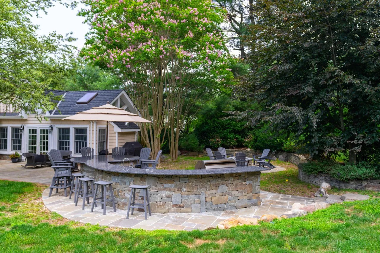 Curved stone outdoor kitchen bar with granite counter and umbrella beside the house