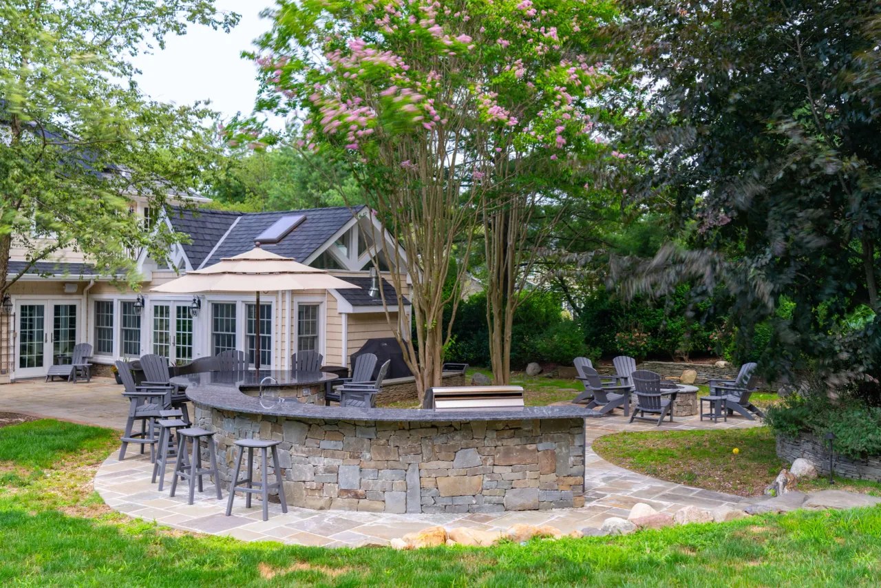 Stone outdoor bar with granite countertop and bar stools beside the house