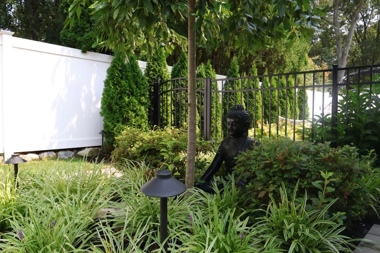 Shaded garden with Asian statuary, layered grasses and path lighting