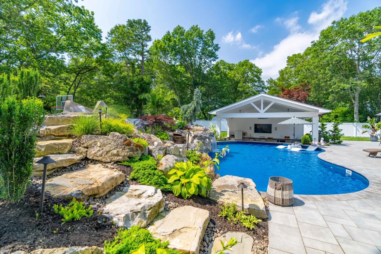 Planted boulder waterfall spilling into a pool beside a pavilion