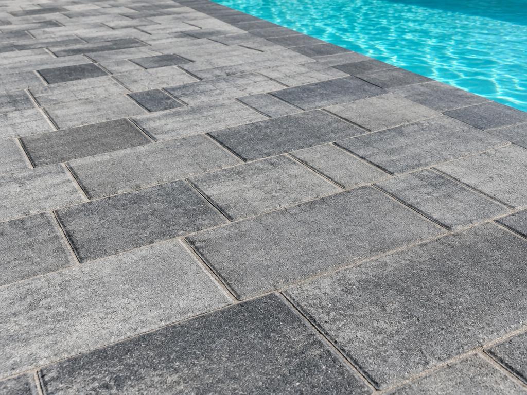 Close-up of textured multi-tone gray concrete pavers beside a pool