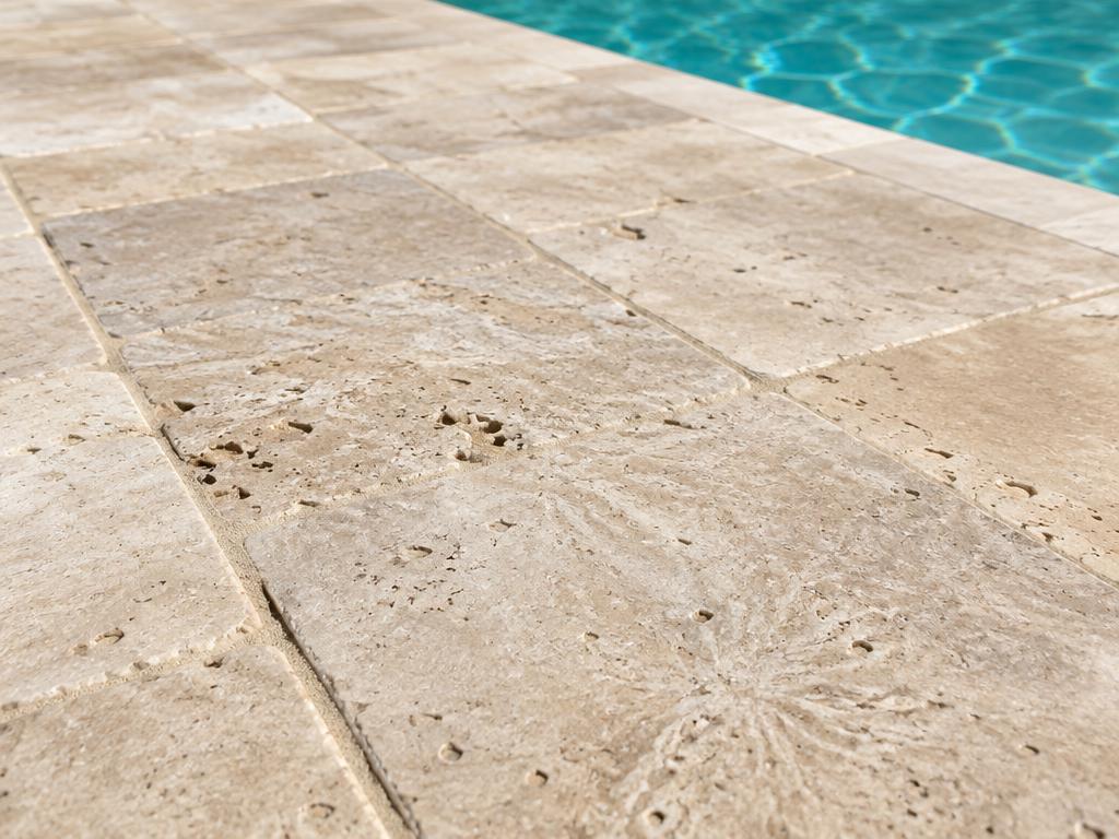 Close-up of ivory tumbled travertine pavers laid beside a pool
