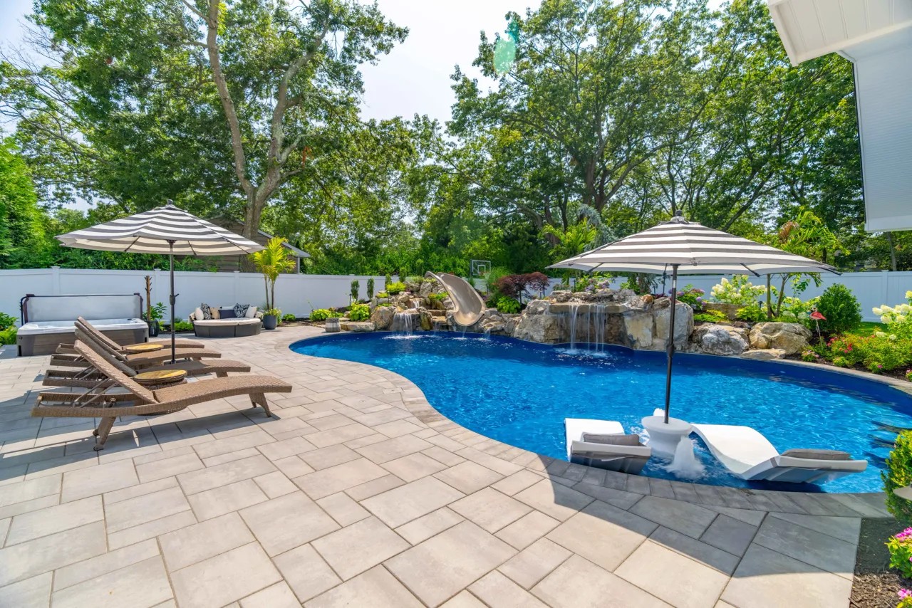 Freeform pool with slide, waterfalls and striped umbrellas on a paver surround
