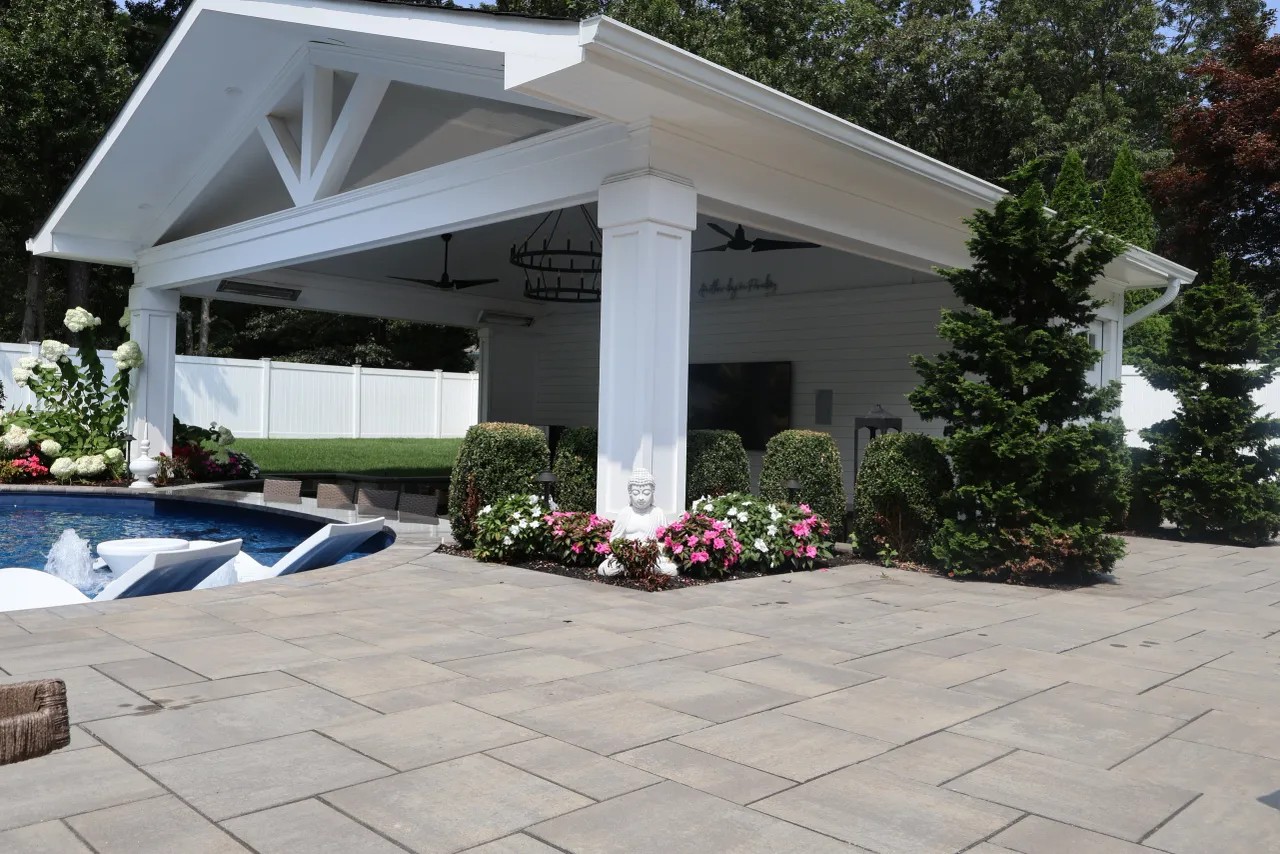 White pool pavilion with stone planter beds on a paver poolside patio