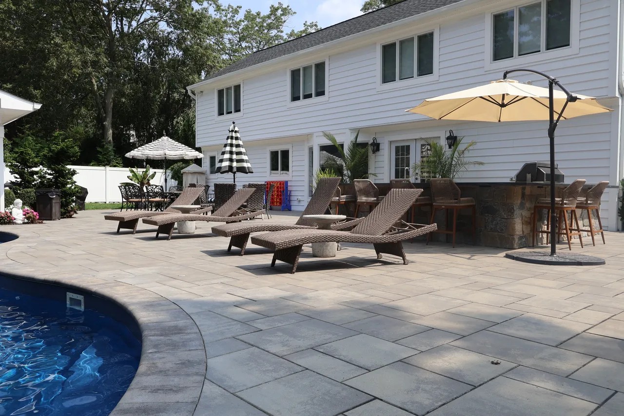 Poolside paver patio with wicker loungers and stone outdoor bar