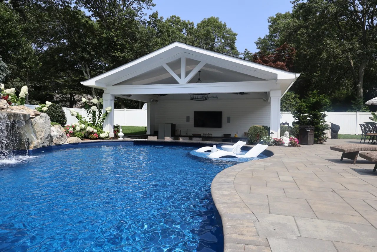 Pool with waterfall grotto and white pavilion beside a paver patio