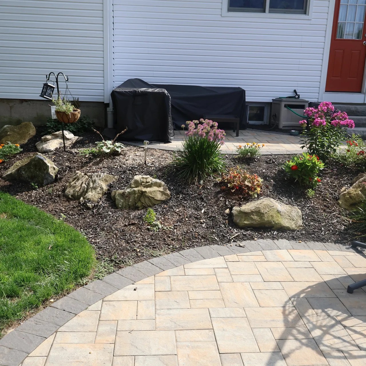 Paver patio edge with boulder planting bed beside the house
