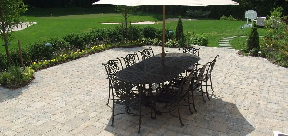 Cast-iron dining set with umbrella on a bluestone patio beside garden beds