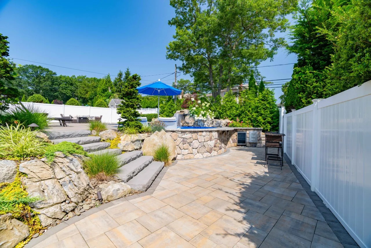 Raised stone spa with outdoor kitchen and bar seating on a paver patio
