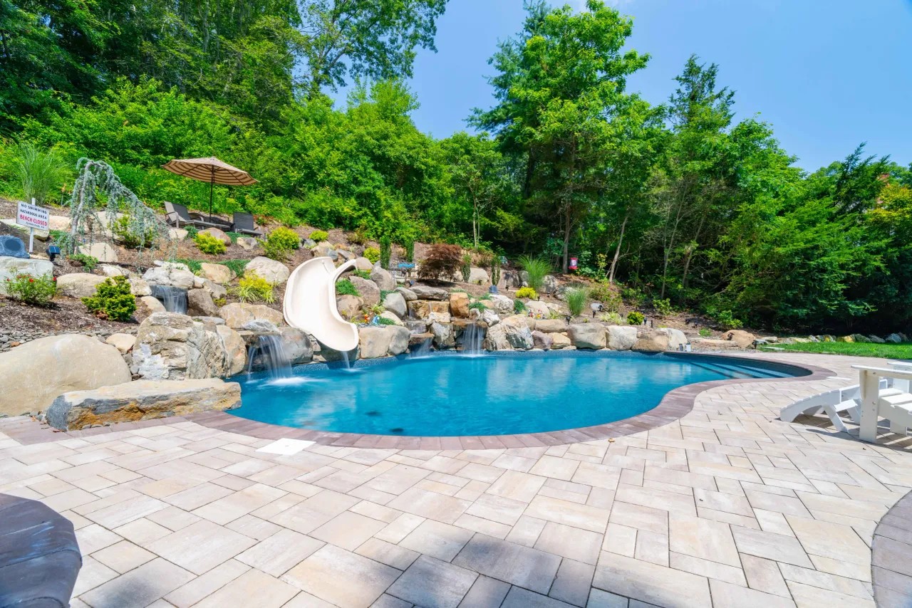 Freeform pool with boulder waterfalls, slide and paver pool surround