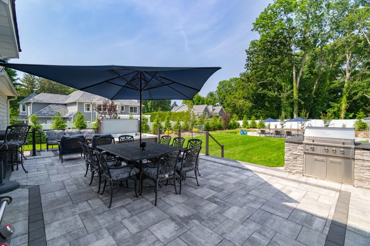 Paver patio dining under an umbrella beside a built-in outdoor kitchen