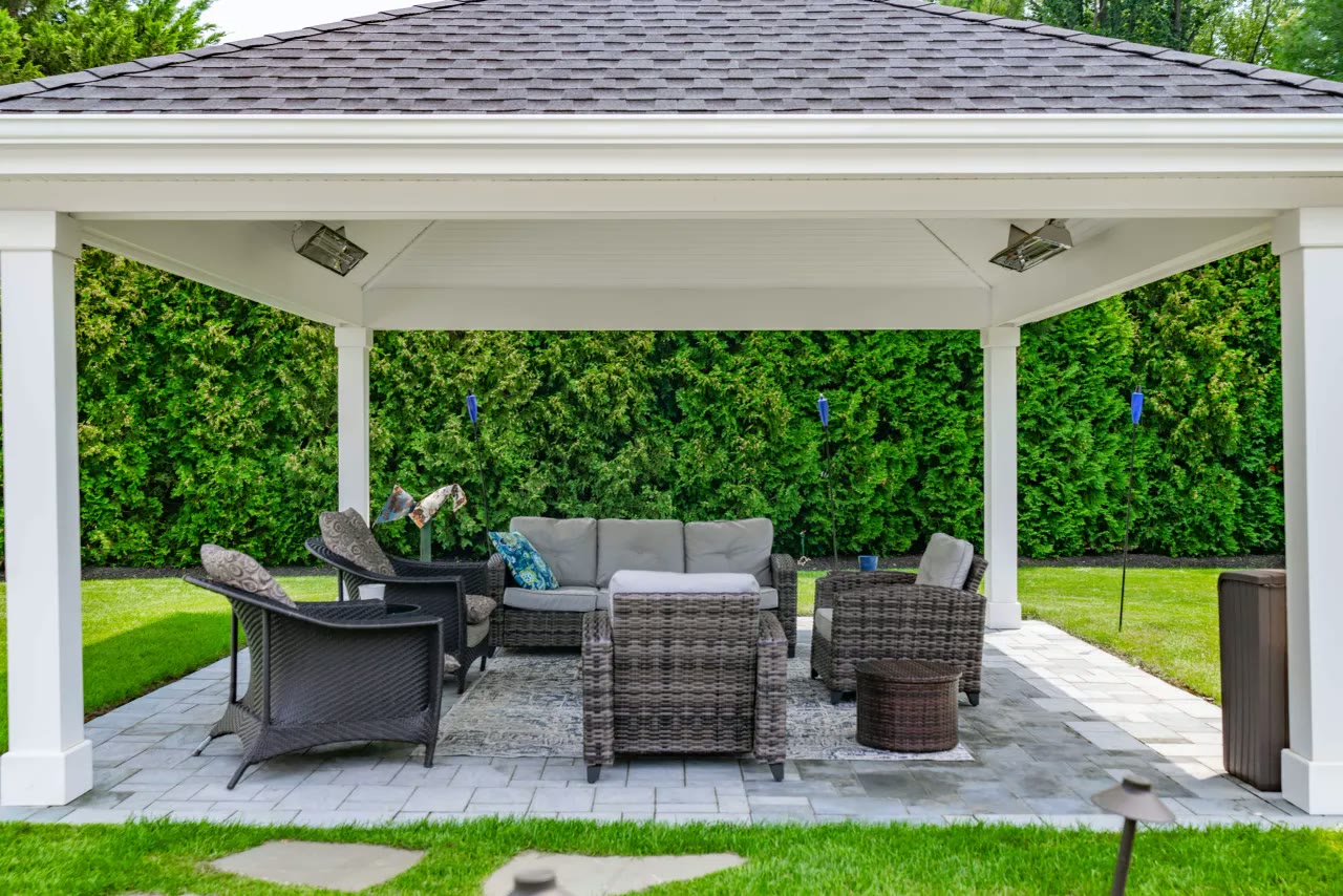 White pavilion with wicker lounge seating and heaters on a paver patio