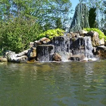 Wide boulder waterfall dropping into a large pond surrounded by trees