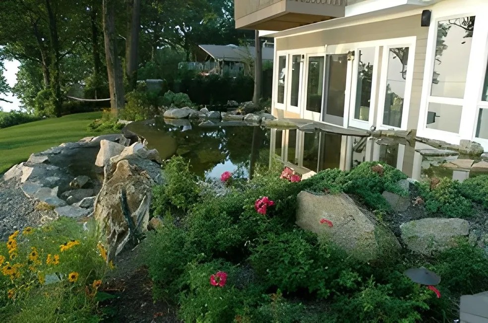 Swimming pond with boulder waterfall beside a waterfront home and lawn