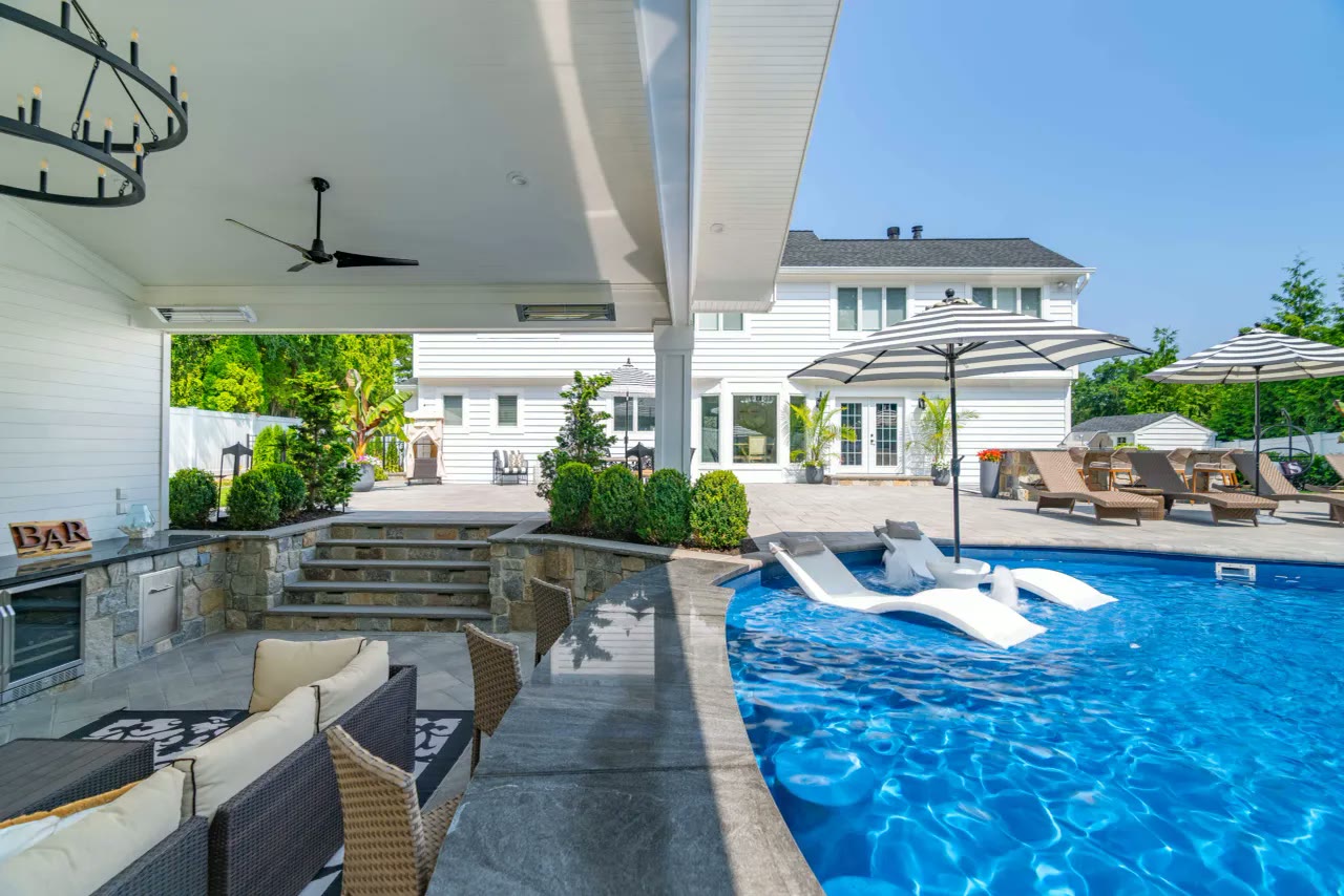 Covered poolside bar and lounge with ceiling fan overlooking a bright blue pool