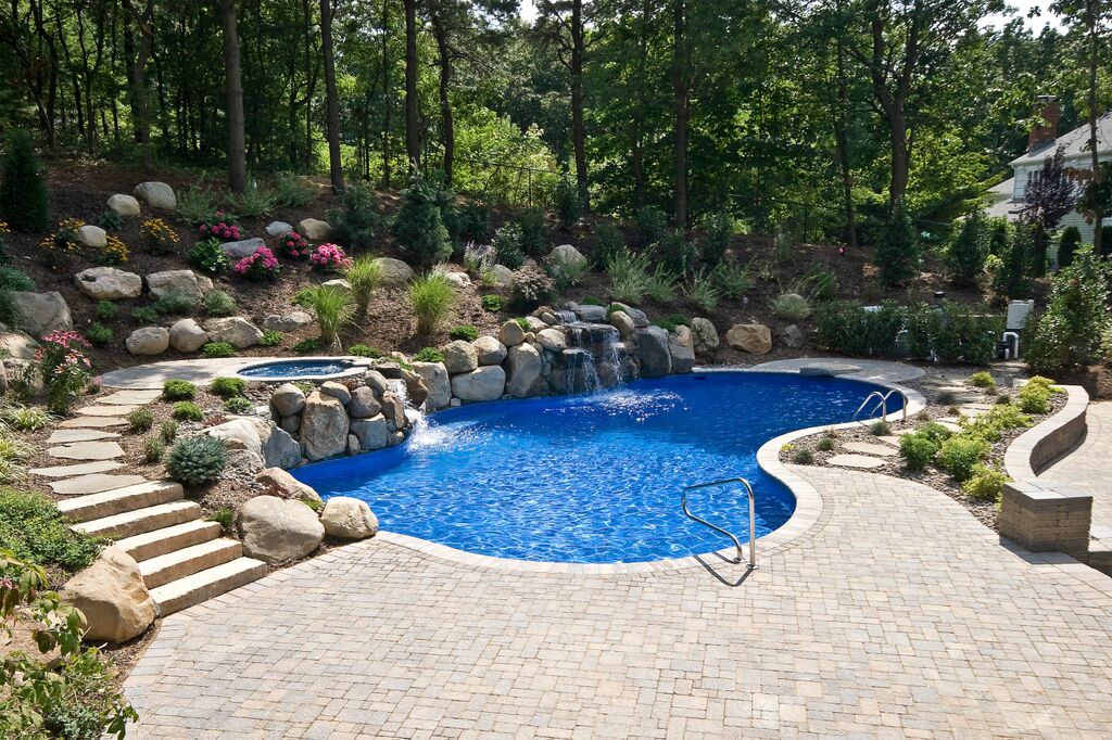 Freeform pool with boulder waterfall, raised spa and stone steps set into a wooded hillside