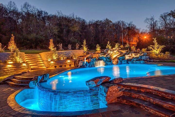 Pool with raised spa, stone waterfalls and slide illuminated at dusk