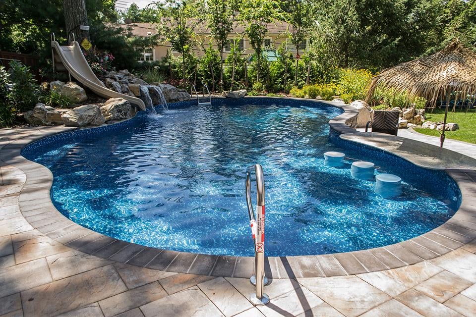 Freeform pool with slide, waterfalls, swim-up bar seating and a paver patio
