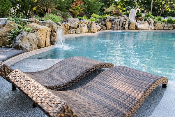 Wicker loungers beside a freeform pool with waterfalls and a slide