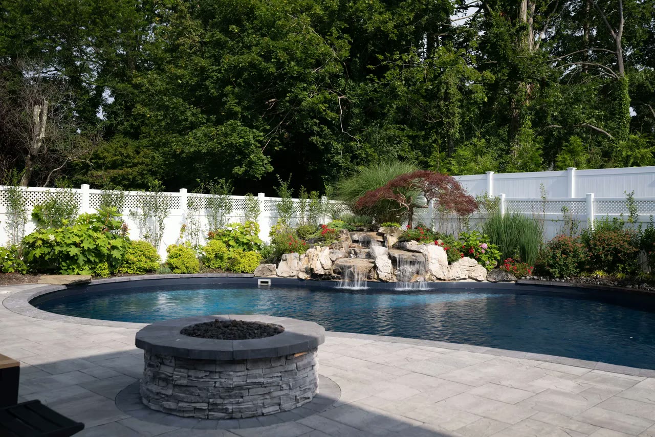 Curved pool with rock waterfall and stone fire pit on a wide paver surround