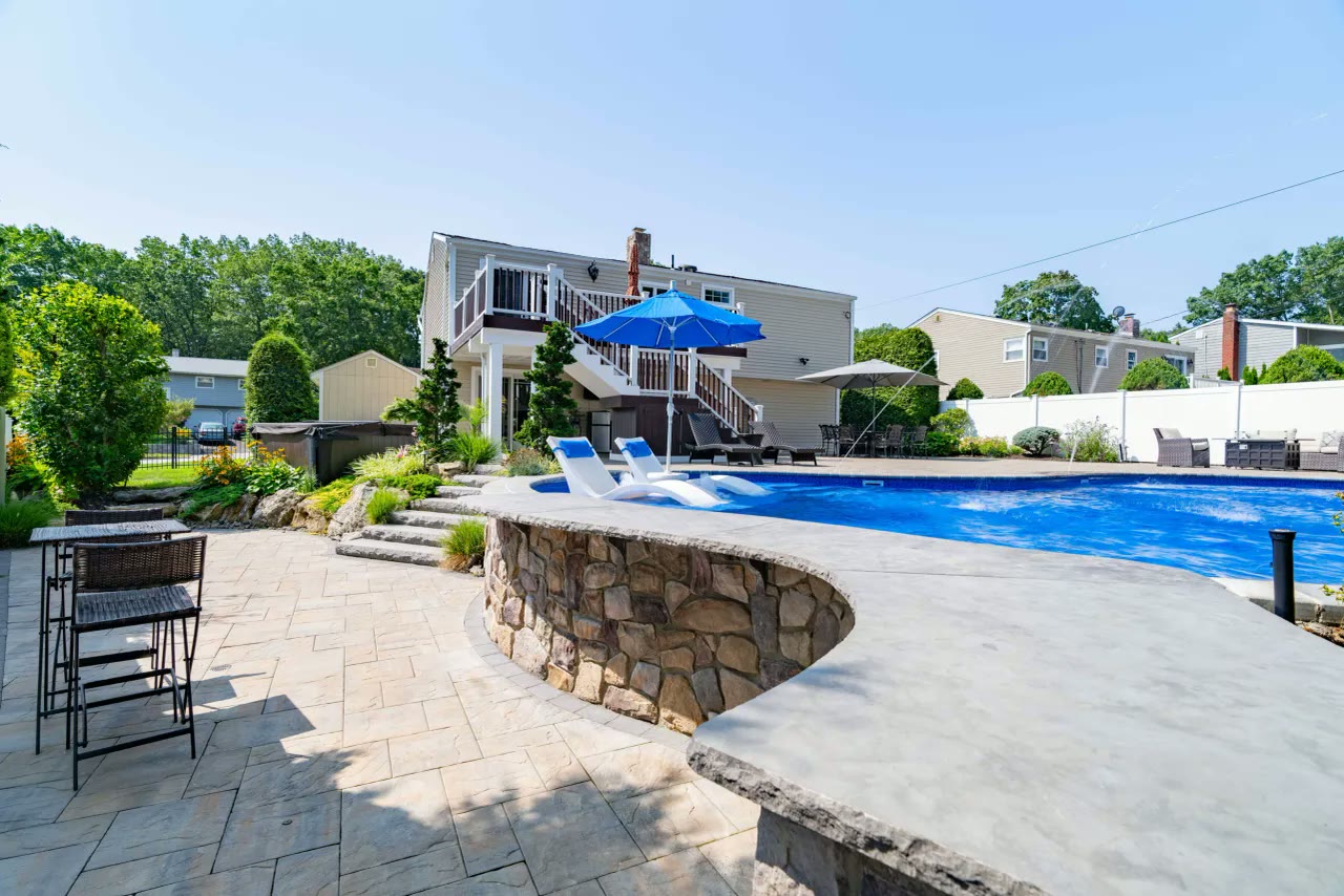Raised pool edge with curved stone wall, tanning ledge loungers and paver pool deck