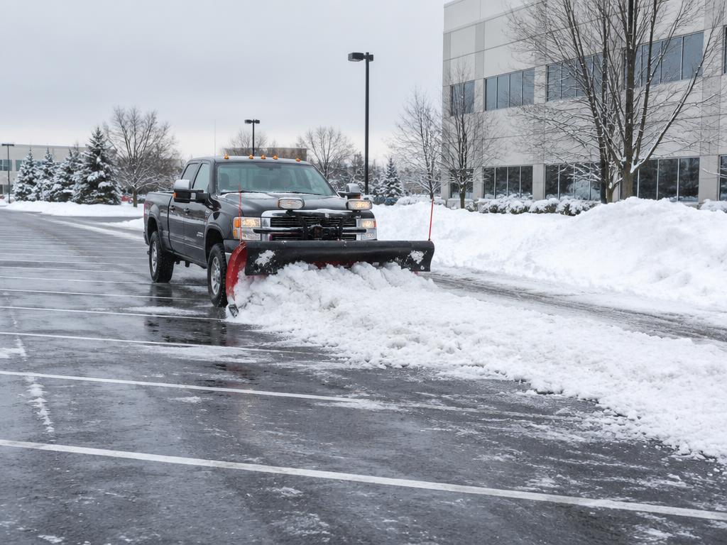 Plow truck pushing snow across a commercial parking lot