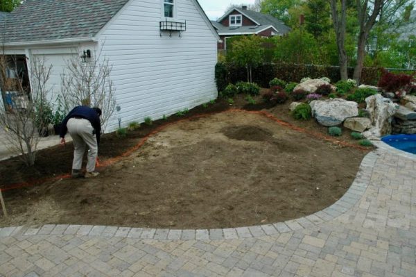 ‘Before’ Landscaping: Here a member of our team is marking out the landscaping areas for behind the waterfall up to the garage. You can see (on the right) the spool and waterfall are already complete. You can also see a small segment of the new patio.